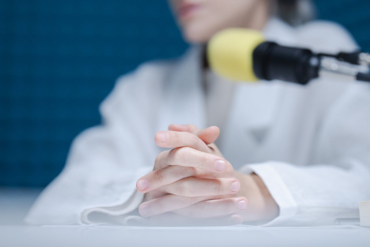 Close-up of hands folded near a microphone in a podcast studio.